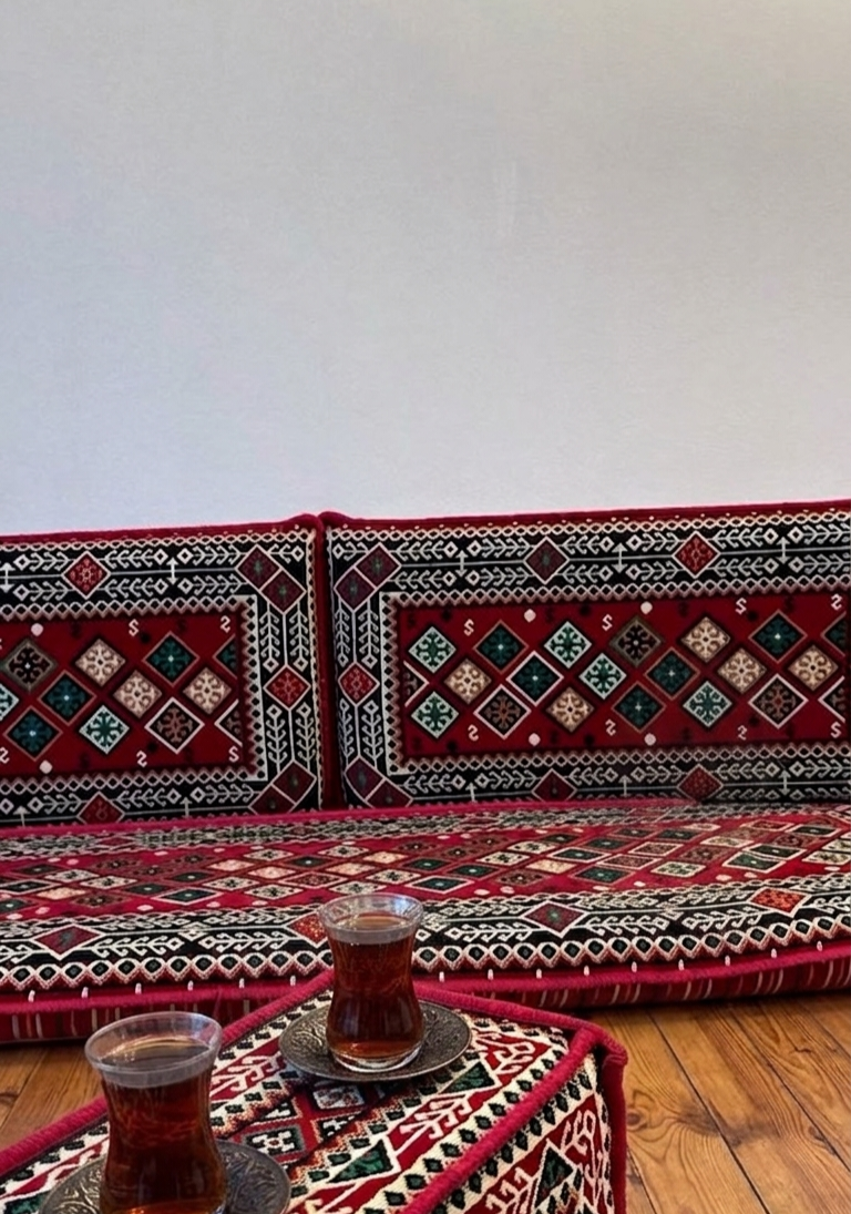 Mosaik-Kissenbezug mit geometrischem Muster in Rot, Schwarz, Weiß und Grün, auf einer traditionellen Sitzbank mit Teegläsern.
