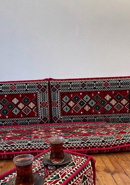 Mosaik-Kissenbezug mit geometrischem Muster in Rot, Schwarz, Weiß und Grün, auf einer traditionellen Sitzbank mit Teegläsern.